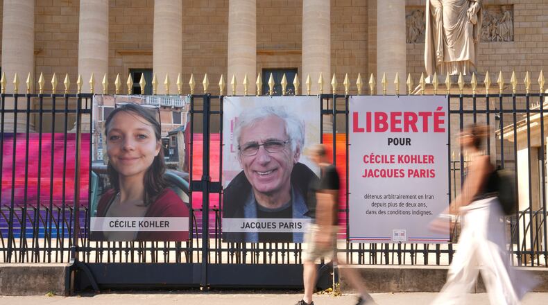 FILE - People walk past the portraits of French nationals Cecile Kohler and Jacques Paris in front of the French National Assembly in Paris on July 3, 2025. (AP Photo/Aurelien Morissard, File)