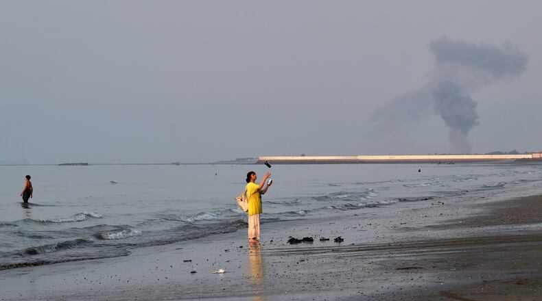 A woman stands at the water's edge along the Strait of Hormuz as a plume of smoke rises in the background following an explosion, off Bandar Abbas, Iran, Monday, July 13, 2026. (Razieh Poudat/ISNA via AP)