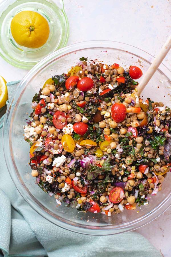 A large salad bowl holds a colorful Lentil Salad with Lemon Vinaigrette that includes lentils, sliced grape tomatoes, kale, peppers and feta.