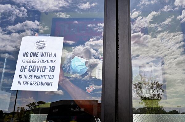 April 25, 2020 Decatur - Julian Douglas, employee, posts a warning sign at the main door as restaurant staff prepare to reopen the restaurant at Bad Daddy's Burger Bar in Decatur on Saturday, April 25, 2020. On Monday, Kemp announced shuttered businesses including barbershops, beauty and nail salons, spas, gyms and bowling alleys could reopen Friday. Movie theaters and restaurant dining rooms can reopen Monday. (Hyosub Shin / Hyosub.Shin@ajc.com)