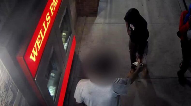 Surveillance footage shows a victim with his back to the camera being robbed at an ATM.