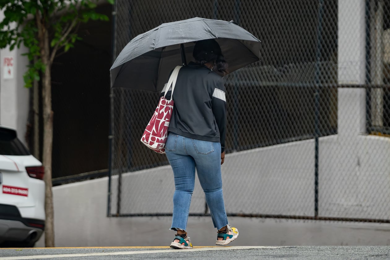 A woman with an umbrella crosses Cone Street during light rain on Friday, May 29, 2026. Rainy days should move out of the area by week's end. (Ben Hendren for the AJC)