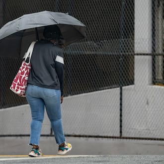 A woman with an umbrella crosses Cone Street during light rain on Friday, May 29, 2026. Rainy days should move out of the area by week's end. (Ben Hendren for the AJC)