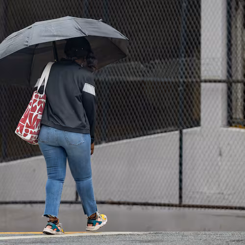 A woman with an umbrella crosses Cone Street during light rain on Friday, May 29, 2026. Rainy days should move out of the area by week's end. (Ben Hendren for the AJC)