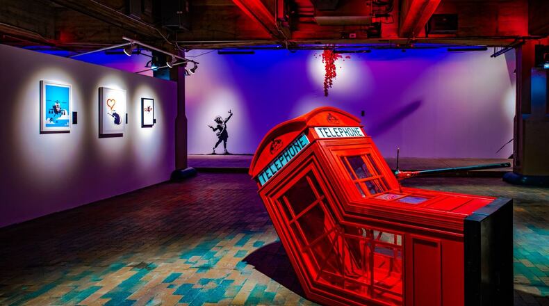 The 2006 Banksy sculpture "Death of a Phone Booth" is framed by three prints and a recreation of the 2020 mural "Valentine's Day" painted by local artists at The Art of Banksy: "Without Limits" exhibition in Underground Atlanta. Lola Scott Art/SEE Global Entertainment