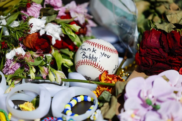 Fans left flowers and other items at the foot of Bobby Cox's statue outside Truist Park. (Arvin Temkar/AJC)