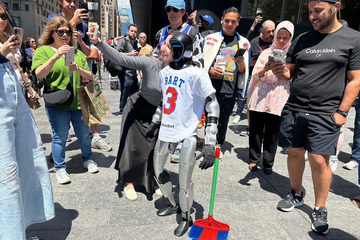 A fan takes a selfie with a robot dressed in New York Knicks gear holding a broom near Madison Square Garden in New York, Monday, June 8, 2026, ahead of Game 3 of the NBA Finals basketball series between the New York Knicks and the San Antonio Spurs. (AP Photo/Ted Shaffrey)