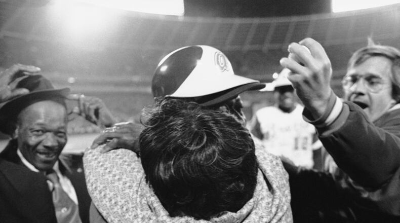 Atlanta Braves' Hank Aaron is embraced by his mother, Estella, as his father Herbert, left, nearly loses his hat and Braves pitcher Tommy House holds the ball that Aaron hit to break Babe Ruth's record, April 8, 1974, in Atlanta. (AP Photo)