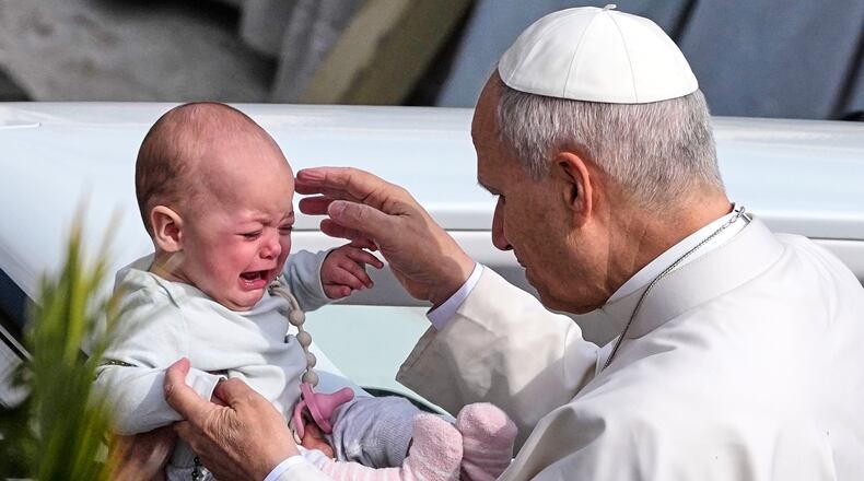 Pope Leo XIV caresses a child after presiding over Mass in St. Peter's Square at the Vatican on the Catholic feast of Palm Sunday, commemorating Jesus' arrival in Jerusalem, Sunday, March 29, 2026. (AP Photo/Alessandra Tarantino)