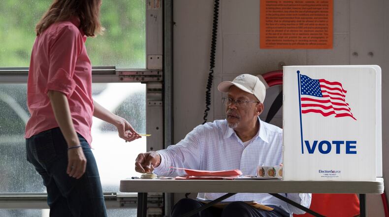 April 18, 2017, Alpharetta - Alpharetta resident Toni Kuhn, left, hands her voter card to Birdel Jackson III, center, at Alpharetta Fire Station 82 in Alpharetta, Georgia, on Tuesday, April 18, 2017. Cobb, Fulton and North DeKalb residents cast ballots today for the highly contested 6th Congressional District race. (DAVID BARNES / DAVID.BARNES@AJC.COM)