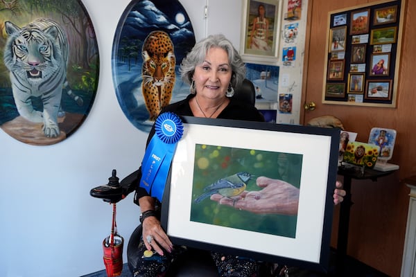 Artist Lora Duguay poses for a portrait in her wheelchair with some of her artwork at home in Clearwater, Fla., on Tuesday, June 10, 2025. (AP Photo/Chris O'Meara)