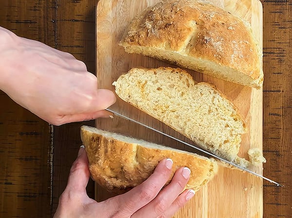Senior AJC Food editor Monti Carlo cuts into a fresh loaf of soda bread on a cutting board set on top of a table.
