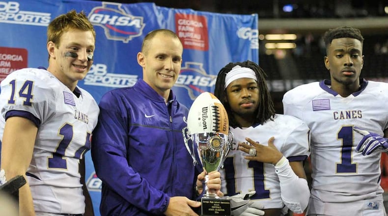Seniors Sean Holton (14, L-R), Xavior Coaxum (11), Trey Creamer (1) hold their championship trophy with Cartersville head coach Joey King after winning the Class AAAA state title game at the Georgia Dome Saturday.