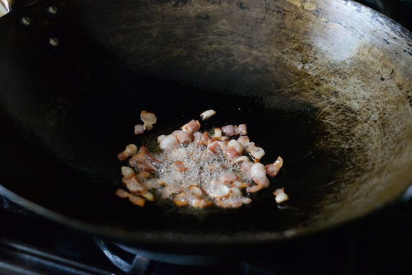 Small pieces of bacon frying in a wok.
