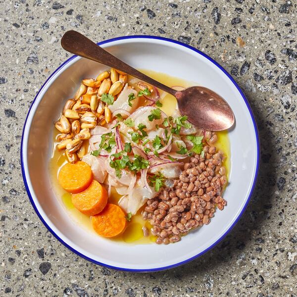 A plate of ceviche from Tio Lucho's sits on a terrazzo table. There are boiled sweet potatoes next to fish swimming in a pale orange leche de tigre.