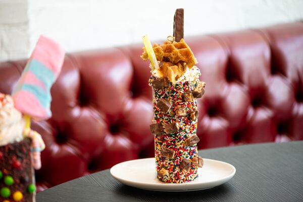 The Sugar Factory Giggles Snickers Milkshake, cookies and cream ice cream blended with toasted peanuts, topped with a caramel waffle, snickers, whipped cream, and sprinkles served in a chocolate covered mug with Snickers pieces and rainbow sprinkles.