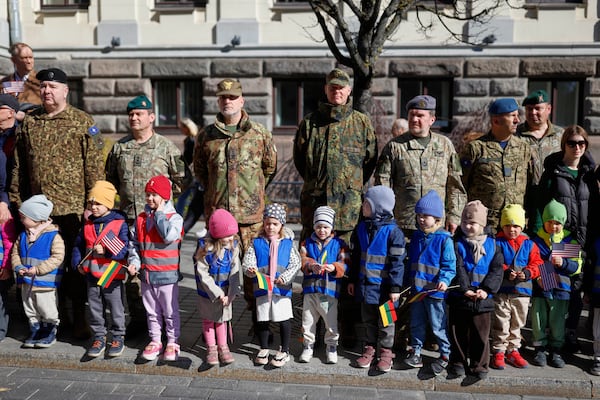 Lithuanian Army soldiers and children with U.S. and Lithuanian flags attend a solemn farewell ceremony at Cathedral Square in Vilnius, Lithuania, Thursday, April 3, 2025 for the US soldiers who died during training exercise. (AP Photo/Mindaugas Kulbis)