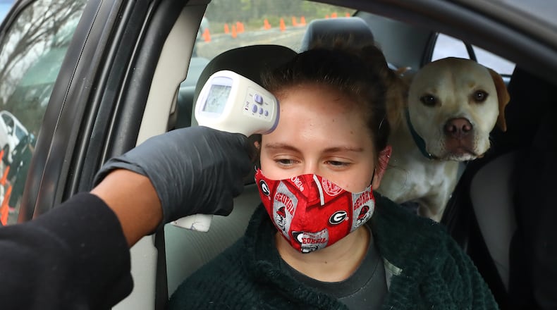 121621 Atlanta: Lauren Wilson has her temperature taken by a health care worker, with her dog Binxy looking on, while getting a COVID test done at the Viral Solutions drive-up vaccinations and testing site on North Druid Hills Road on Thursday, Dec 16, 2021, in Atlanta. Curtis Compton / Curtis.Compton@ajc.com