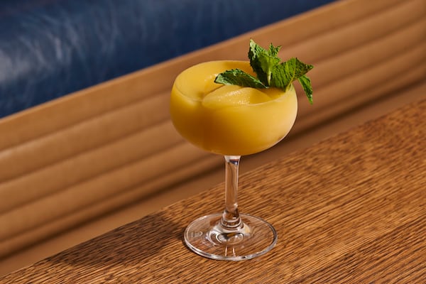 A brightly colored frozen cocktail garnished with a mint leaf on a wooden tabletop.