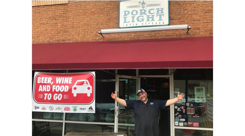 Porch Light Latin Kitchen chef-owner Andre Gomez stands at the entrance to his Smyrna restaurant. Gomez has been heartened by the support from his customers, some who order from him multiple times a week. LIGAYA FIGUERAS / LIGAYA.FIGUERAS@AJC.COM