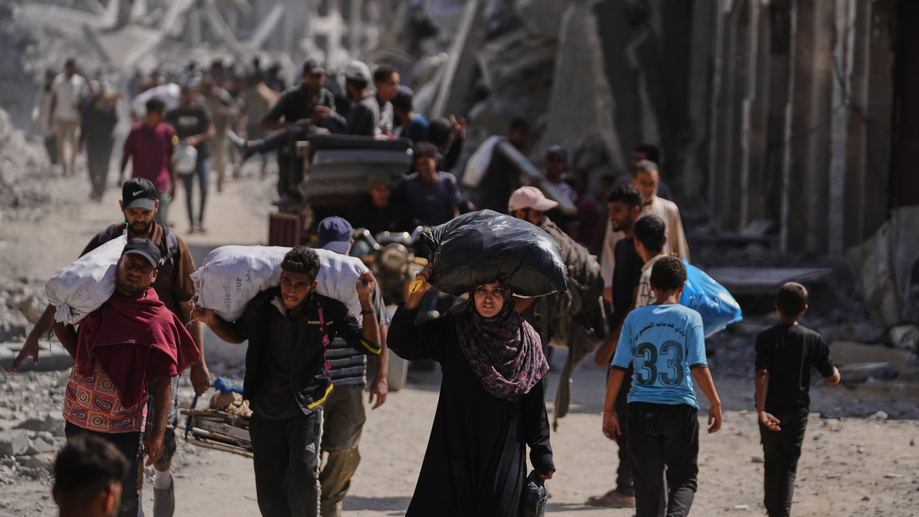 Displaced Palestinians walk with their belongings past destroyed buildings as they return to their homes in Khan Younis, southern Gaza Strip, Friday, Oct. 10, 2025, after Israel and Hamas agreed to a pause in their war and the release of the remaining hostages. (AP Photo/Jehad Alshrafi)