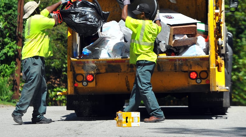 May 10, 2012 Tucker, GA: DeKalb County sanitation workers Cimon Bridges, left, and Larry Wyatt dump trash into the truck May 10, 2012. BRANT SANDERLIN / AJC.COM