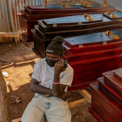 Djakisa Christian, 18, a funeral home manager, sits in front of coffins for sale at his shop in Bunia, Congo, Friday, May 22, 2026. (AP Photo/Moses Sawasawa)
