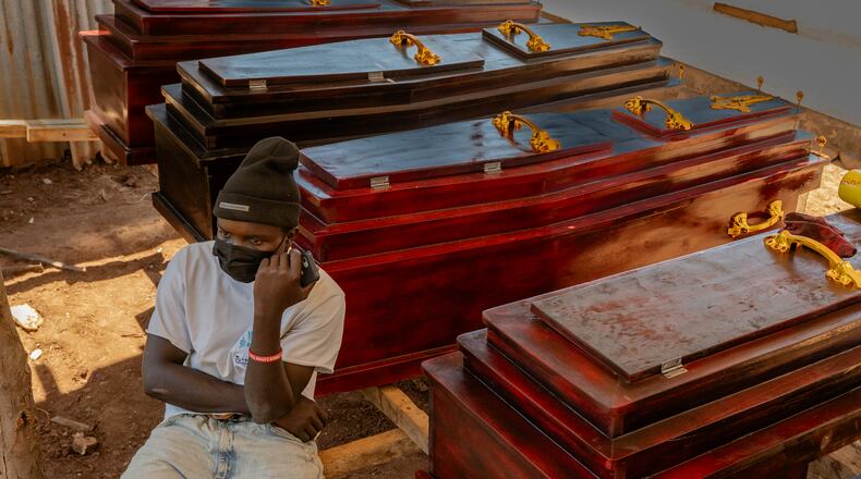 Djakisa Christian, 18, a funeral home manager, sits in front of coffins for sale at his shop in Bunia, Congo, Friday, May 22, 2026. (AP Photo/Moses Sawasawa)
