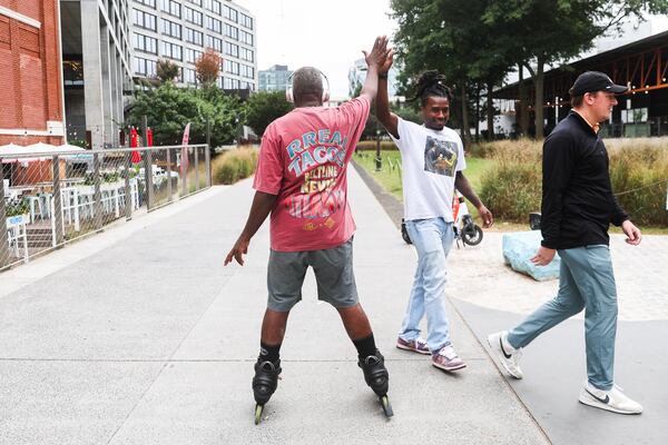 Kevin Randolph high fives a stranger outside of Rreal Tacos on the Beltline across from Ponce City Market in Atlanta. Kevin Randolph became well known for being a friendly rollerblader serenading people along the Beltline. (Abbey Cutrer / AJC)
