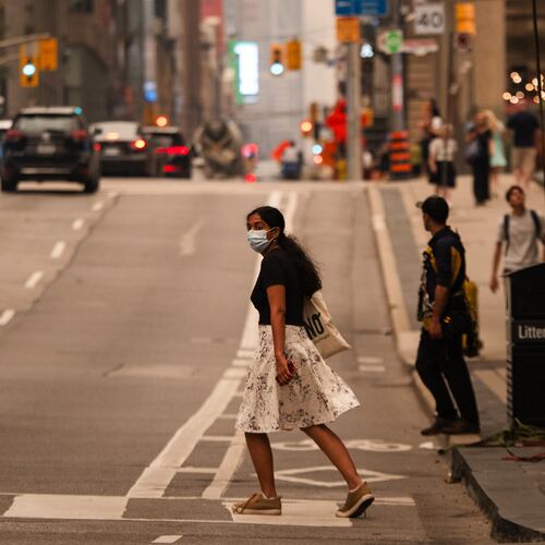 A woman wearing a mask crosses the street in Toronto as wildfire smoke fills the city, on Wednesday, July 15, 2026. (Laura Proctor/The Canadian Press via AP)