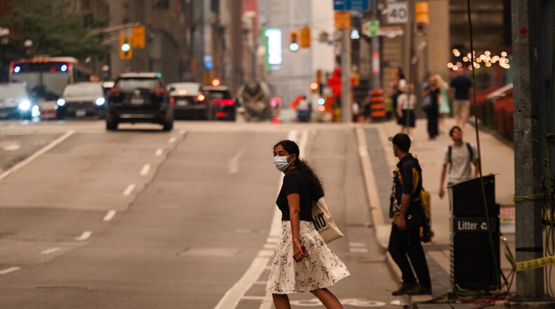 A woman wearing a mask crosses the street in Toronto as wildfire smoke fills the city, on Wednesday, July 15, 2026. (Laura Proctor/The Canadian Press via AP)