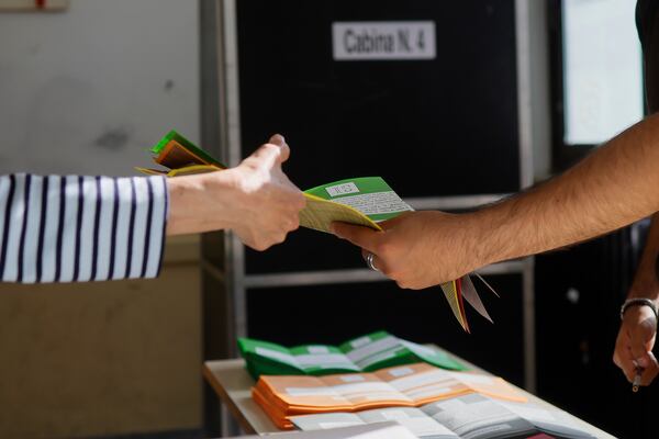 Ballot papers are handed over to a citizen, left, to vote on referendums on citizenship and job protections, at a polling station in Rome, Sunday, June 8, 2025. (Cecilia Fabiano/LaPresse via AP)