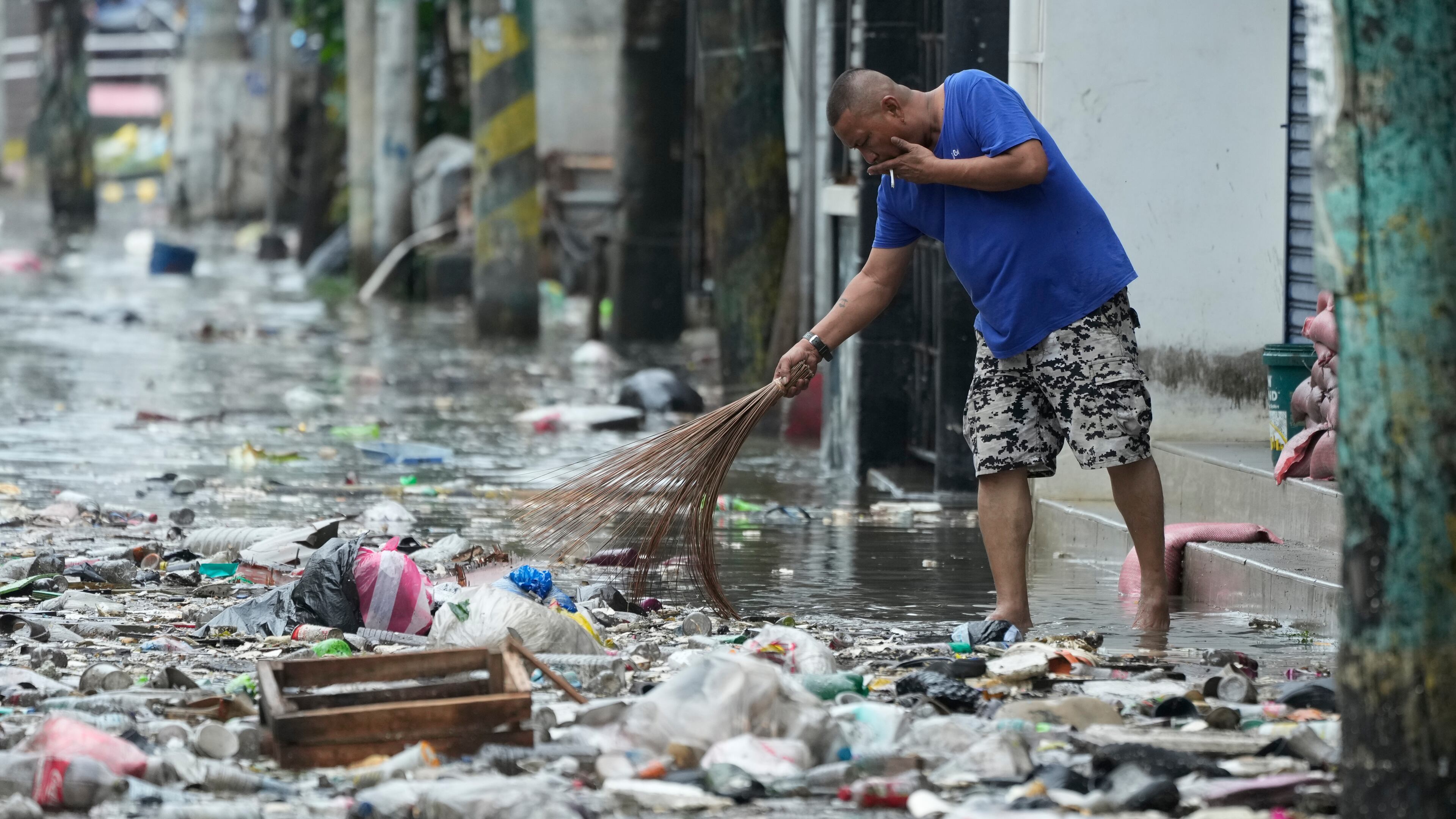 A man cleans garbage along a flooded street due to Typhoon Fung-wong and high tide on Monday, Nov. 10, 2025, in Navotas, Philippines. (AP Photo/Aaron Favila)