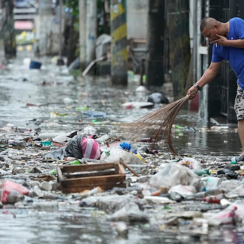 A man cleans garbage along a flooded street due to Typhoon Fung-wong and high tide on Monday, Nov. 10, 2025, in Navotas, Philippines. (AP Photo/Aaron Favila)