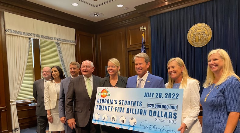 Gov. Brian Kemp holds a check representing how much money the Georgia Lottery has raised for education since 1993. Among those with Kemp at the news conference on Thursday, July 28, 2022, are Technical College System of Georgia Commissioner Greg Dozier (third from left), University System of Georgia Chancellor Sonny Perdue (fourth from left), Gretchen Corbin (fifth from left), CEO and president of the Georgia Lottery, and Kemp's wife, Marty (second from right). (Vanessa McCray / Vanessa.McCray@ajc.com)