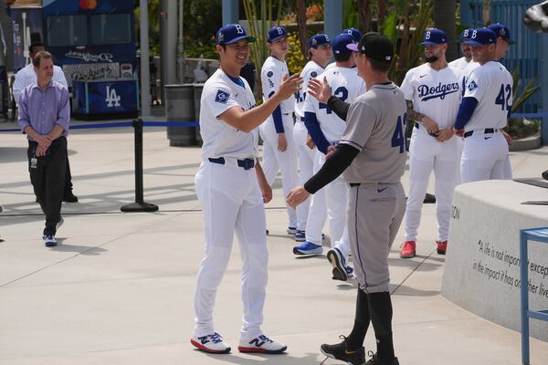Los Angeles Dodgers' Shohei Ohtani, left, shakes hands with a member of the Colorado Rockies at Dodger Stadium during an event to commemorate Jackie Robinson Day before a baseball game Tuesday, April 15, 2025, in Los Angeles. (AP Photo/Damian Dovarganes)