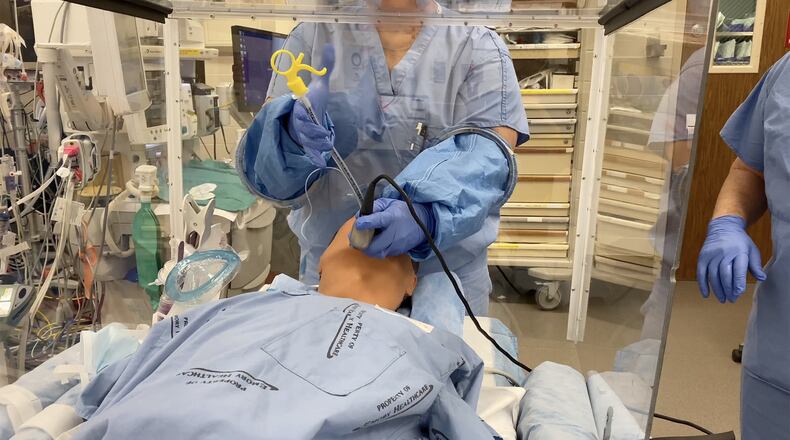 Dr. Cinnamon Sullivan, an assistant professor of anesthesiology at Emory University School of Medicine, and her colleague Dr. Jeremy Collins, an associate professor of anesthesiology, demonstrate how the four-sided box can be used to perform procedures such as intubating a patient who needs to be placed on a ventilator, and create a protective barrier for health care workers. CONTRIBUTED BY EMORY