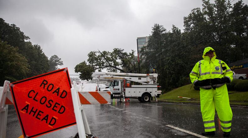 An officer keeps watch as crews work to clear a tree that fell on power lines on Hammond Drive, Monday, Sept. 11, 2017, in Sandy Springs, Ga.  BRANDEN CAMP/SPECIAL