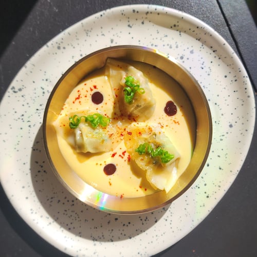 Three dumplings are artfully arranged in a bowl with a creamy sauce and garnished with circles of green onion.