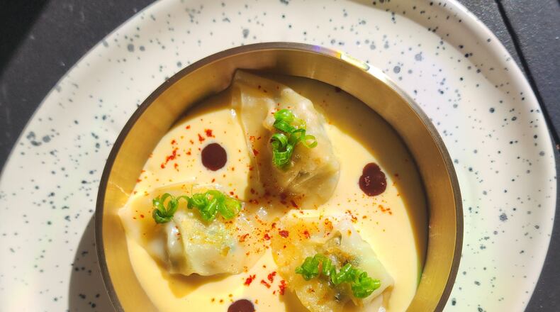 Three dumplings are artfully arranged in a bowl with a creamy sauce and garnished with circles of green onion.