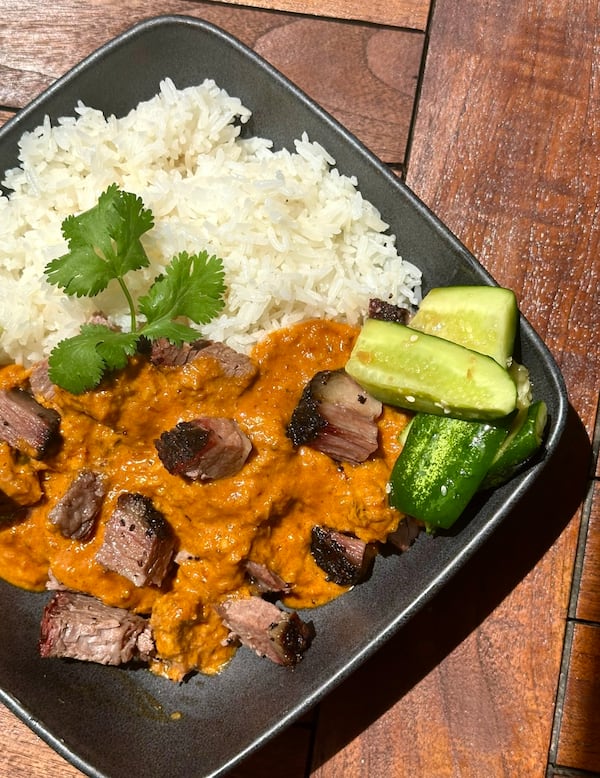 Smoked brisket rendang on a plate accompanied by white rice, cucumbers and garnished with a cilantro stem.