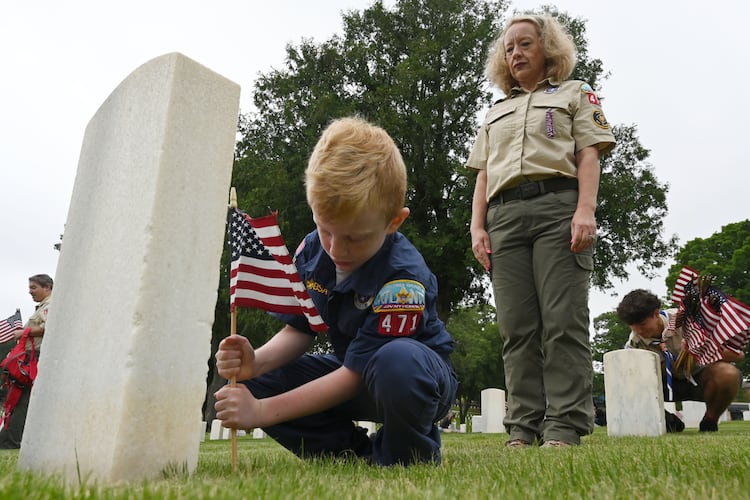 Cade Larkin, 9, places a flag as his mother, Ingle Larkin, looks on during the Memorial Day Flag Placement event at Marietta National Cemetery on Saturday, May 23, 2026, in Marietta. Scouting groups in the community place more than 18,000 U.S. veteran grave flags at Marietta National Cemetery each year on the Saturday before Memorial Day, helping prepare for Monday’s ceremony. The long-running service project—organized with the National Memorial Day Association of Georgia—also gives youth and adults an opportunity to honor fallen service members and learn about their sacrifices and the area’s history. (Hyosub Shin/AJC)