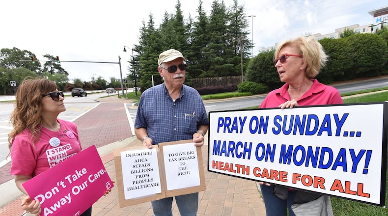 Protesters, from left, Anita Tucker, Michael Blundell and June Krise display signs opposing the new Senate health care repeal bill outside U.S. Sen. Johnny Isakson’s office on Friday. HYOSUB SHIN / HSHIN@AJC.COM