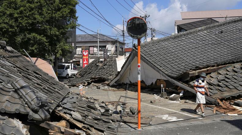 A person walks past the houses collapsed in an earthquake in Yatsushiro, Kumamoto Prefecture, southern Japan, Friday, July 31, 2026. (Koji Harada/Kyodo News via AP)