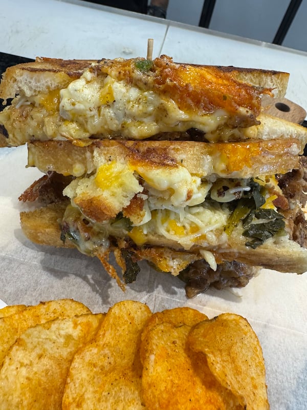 A large grilled cheese cut in half, with the halves stacked on top of each other, with mac and cheese and collard greens visibly incorporated into the melted cheese.