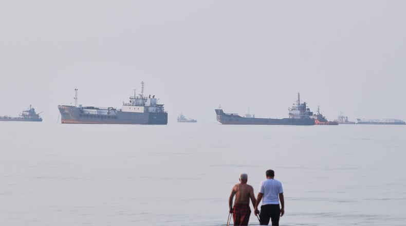 Two men wade in the waters of the Strait of Hormuz with vessels anchored in the background, off Bandar Abbas, Iran, Sunday, July 12, 2026. (Razieh Poudat/ISNA via AP)