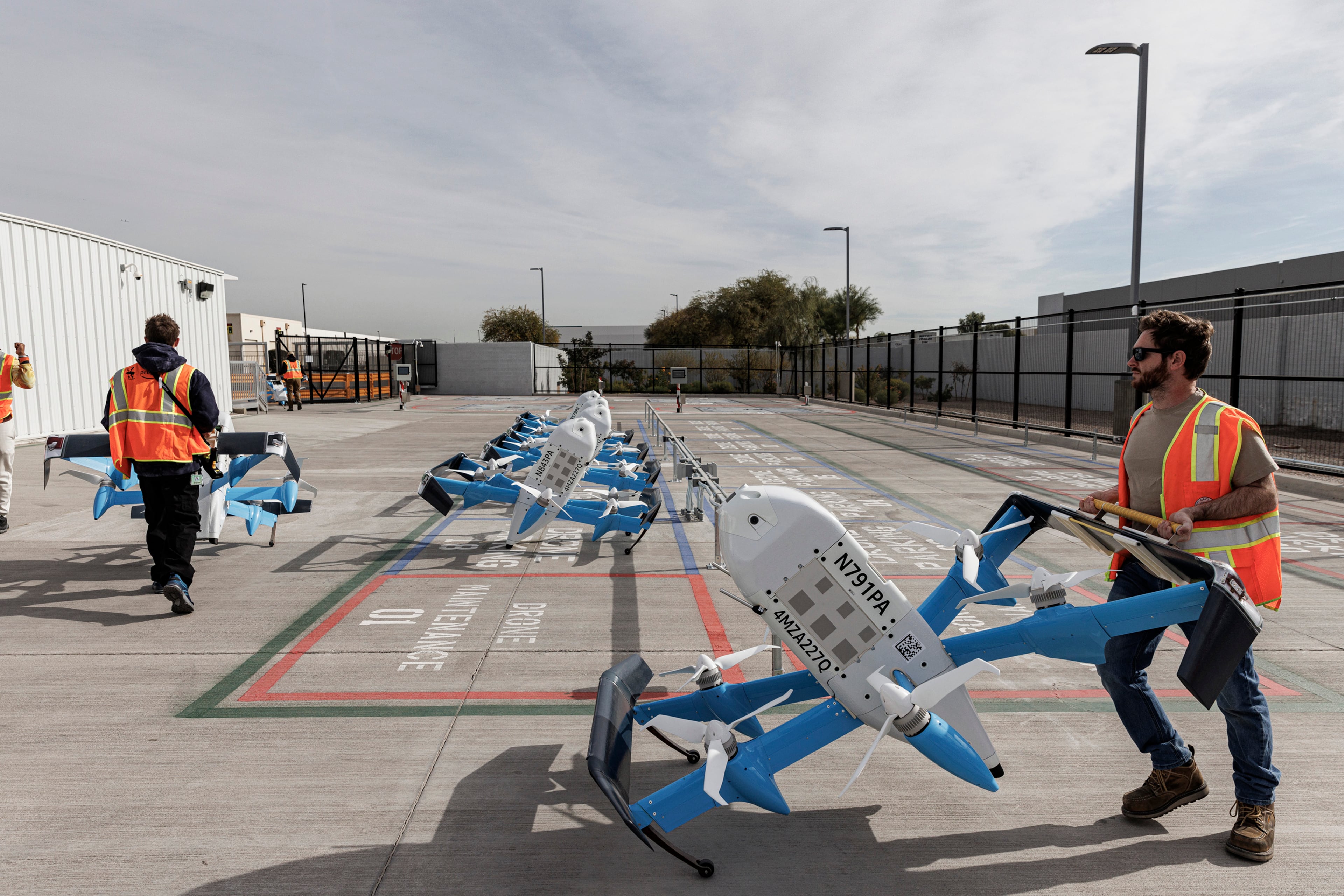 Amazon employees handle delivery drones at the Amazon Same Day Delivery site in Tolleson, Arizona, Dec. 16, 2024. A recent visit to the company’s overhauled drone delivery program in Arizona left some impressed by the drones, but skeptical that the public will welcome them. (Adriana Zehbrauskas/The New York Times)