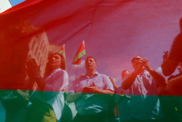 FILE – Belarusian government supporters, seen through a state flag, listen to a speaker at a rally at Independence Square in Minsk, Belarus, on Aug. 16, 2020. (AP Photo, File)