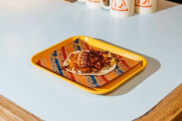 A single breakfast taco sits flat on a tray on a mostly empty table