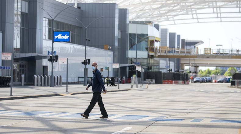 A man wearing a mask walks along a crosswalk in a nearly empty airport arrivals entrance at Hartsfield-Jackson International Airport in Atlanta, Tuesday, April 14, 2020. (ALYSSA POINTER / ALYSSA.POINTER@AJC.COM)